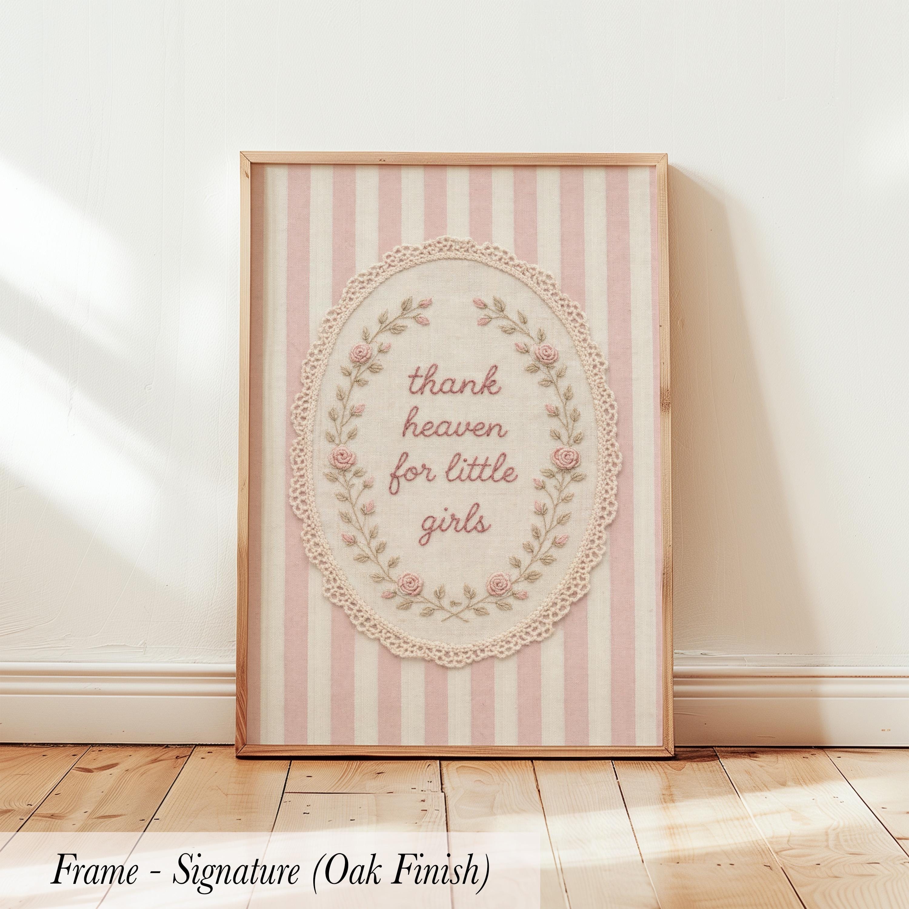 A framed print with a pink and white striped background and a lace border, featuring the text "Thank heaven for little girls" in a decorative font.