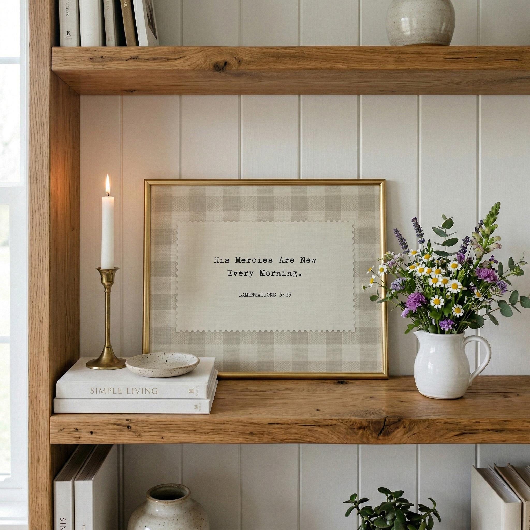 a wooden bookshelf with a framed quote, a white vase with flowers, and a lit candle.