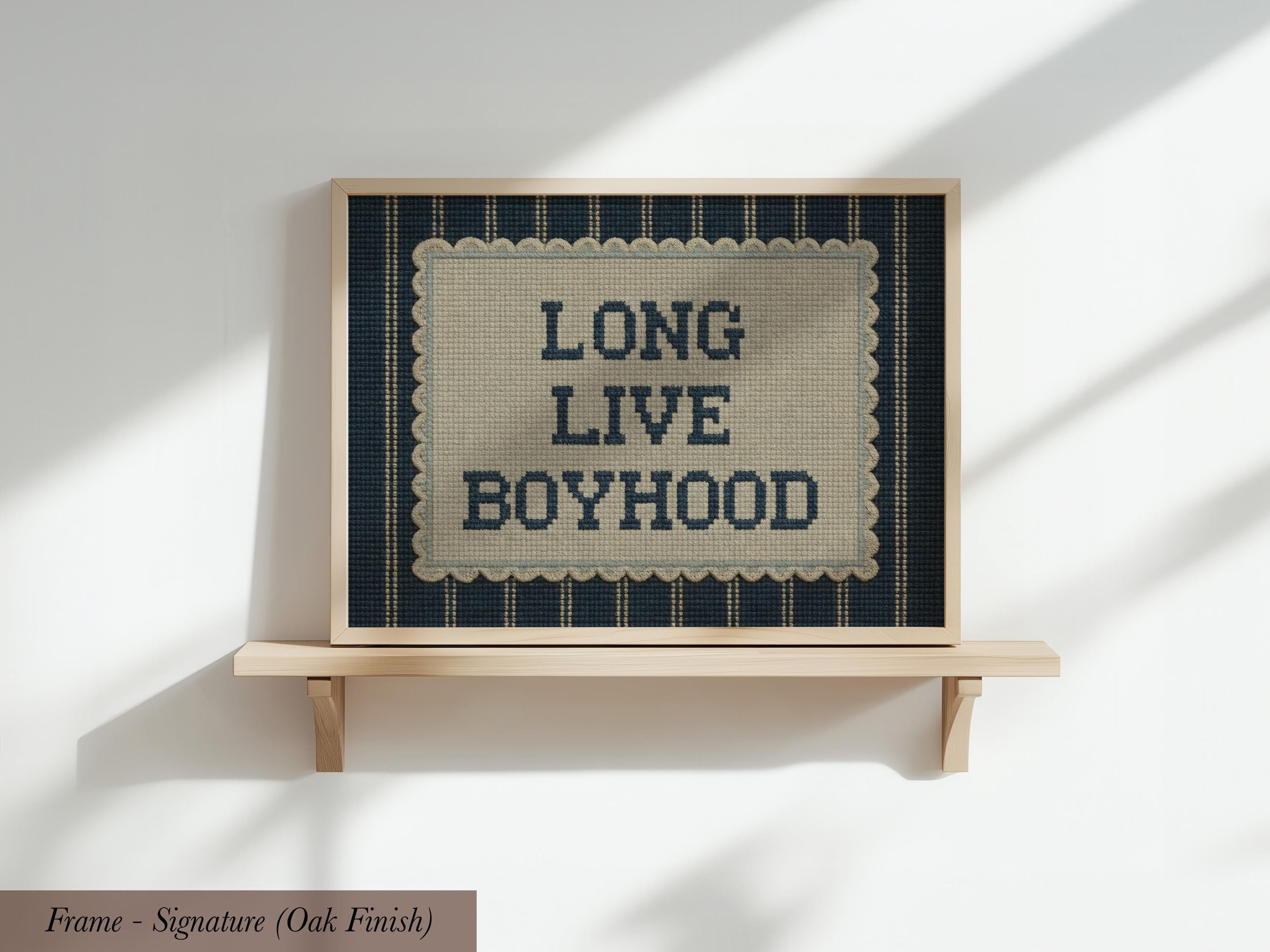 a framed sign with the text "LONG LIVE BOYHOOD" on it, displayed on a wooden shelf against a white wall.