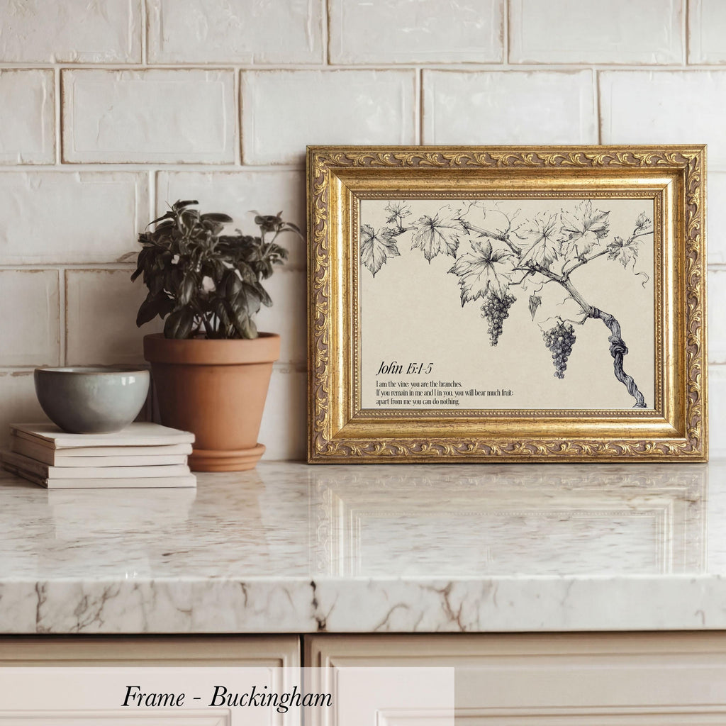 A framed print of a vineyard with grapes is displayed on a marble countertop, accompanied by a potted plant, a stack of books, and a bowl.