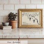 A framed print of a vineyard with grapes is displayed on a marble countertop, accompanied by a potted plant, a stack of books, and a bowl.