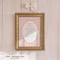A framed print with a pink and white checkered background hangs on a wooden wall. The frame is gold and has a bow on top.