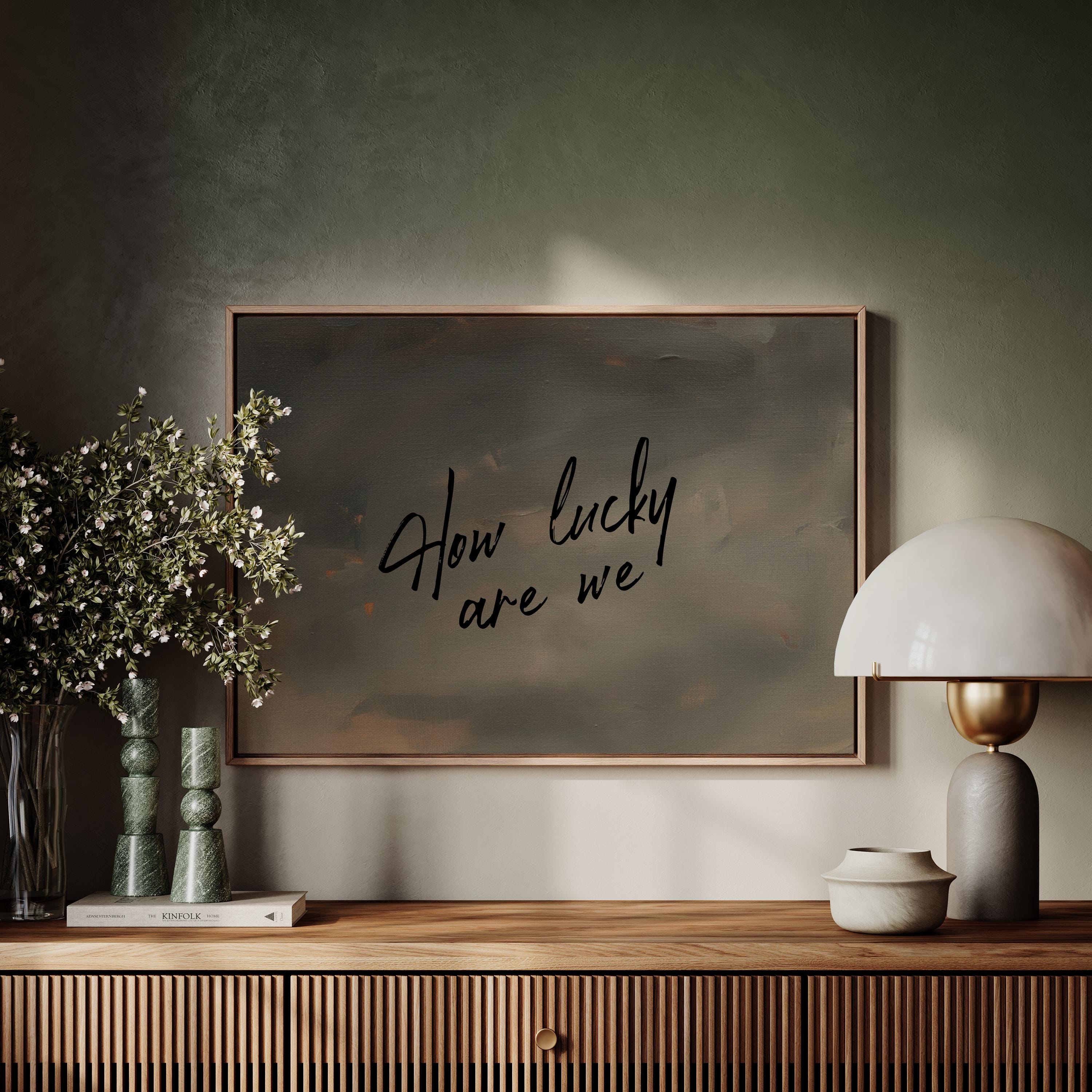 a wooden shelf with a framed artwork hanging on the wall above it, a lamp, and some decorative items such as a vase with flowers and a book.
