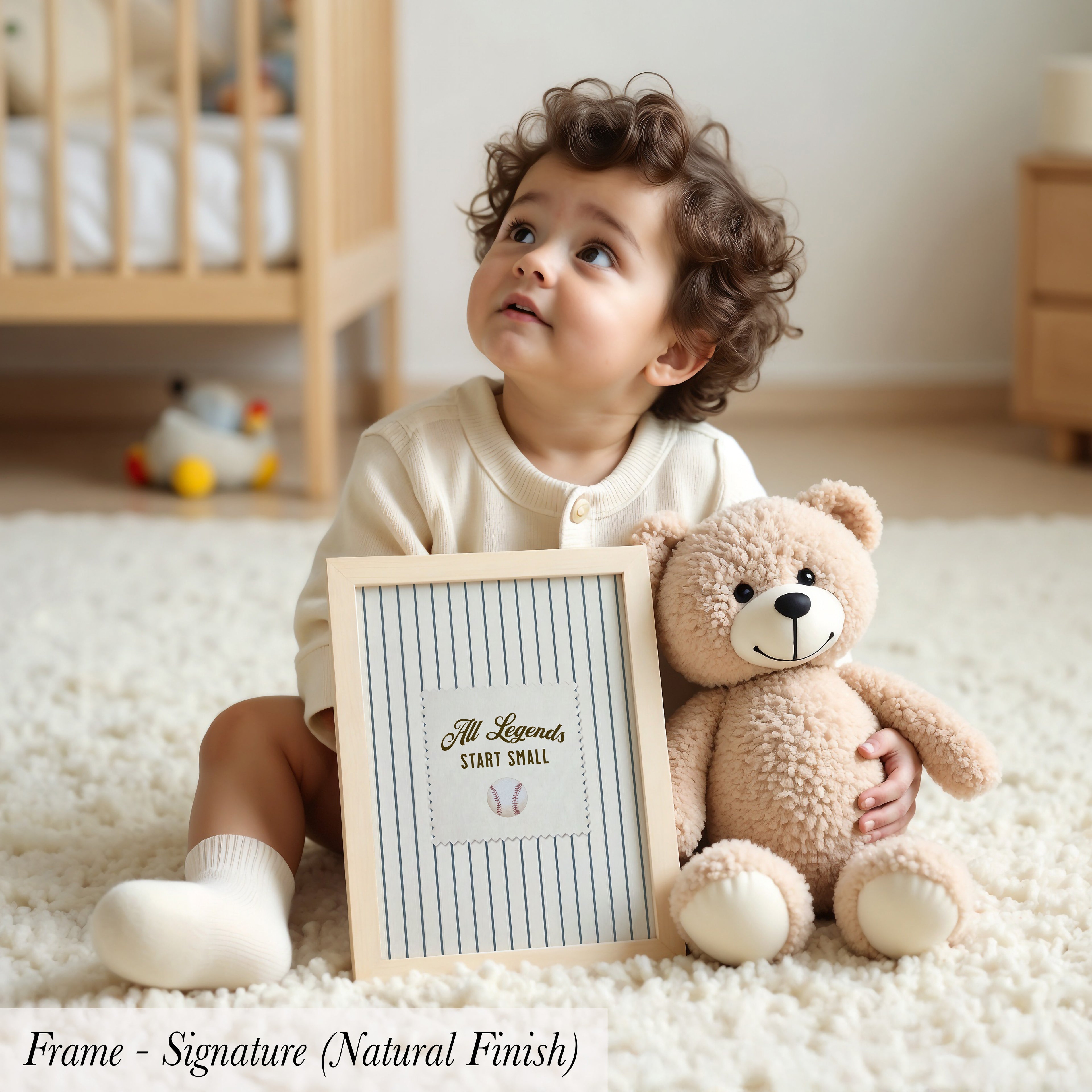 A young child sits on the floor, holding a framed sign that says "All Legends Start Small". Next to the child is a teddy bear.