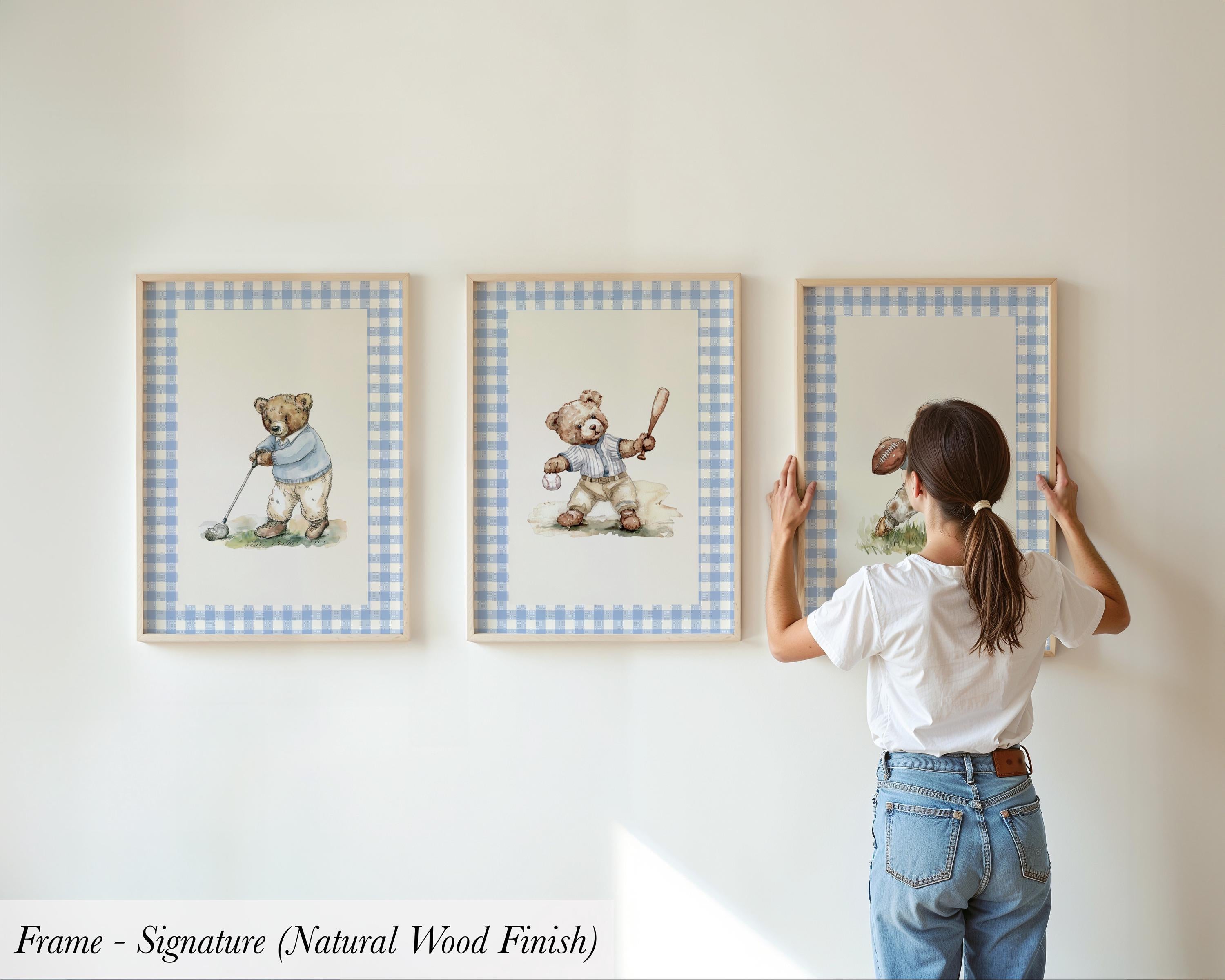 A woman is hanging three framed pictures on a wall, each depicting a teddy bear in different poses.