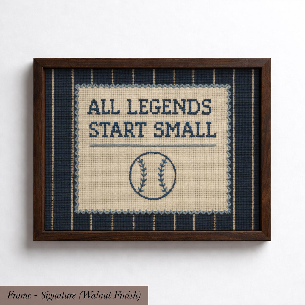 a framed cross-stitch design with the text "ALL LEGENDS START SMALL" and a baseball motif.