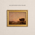 May include: A rectangular landscape painting in a decorative gold frame labeled BUCKINGHAM GOLD FRAME. The artwork depicts a dark cluster of trees near a calm body of water under a soft, hazy pink and orange sunset sky with muted earth tones.
