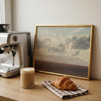 a cozy scene with a painting of a cloudy sky, a croissant, and a cup of coffee on a wooden table.