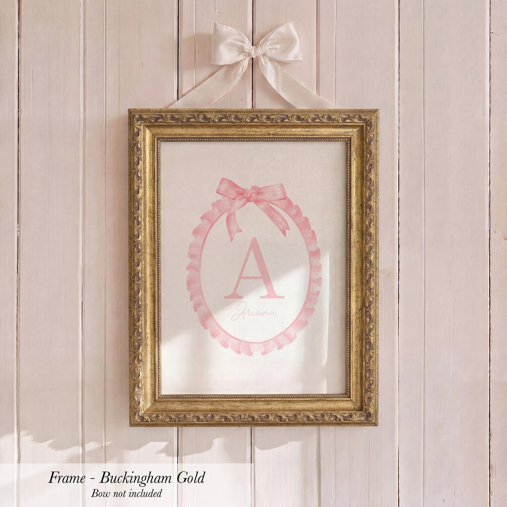 a gold-framed picture hanging on a wooden wall, with a pink bow tied around the top of the frame.