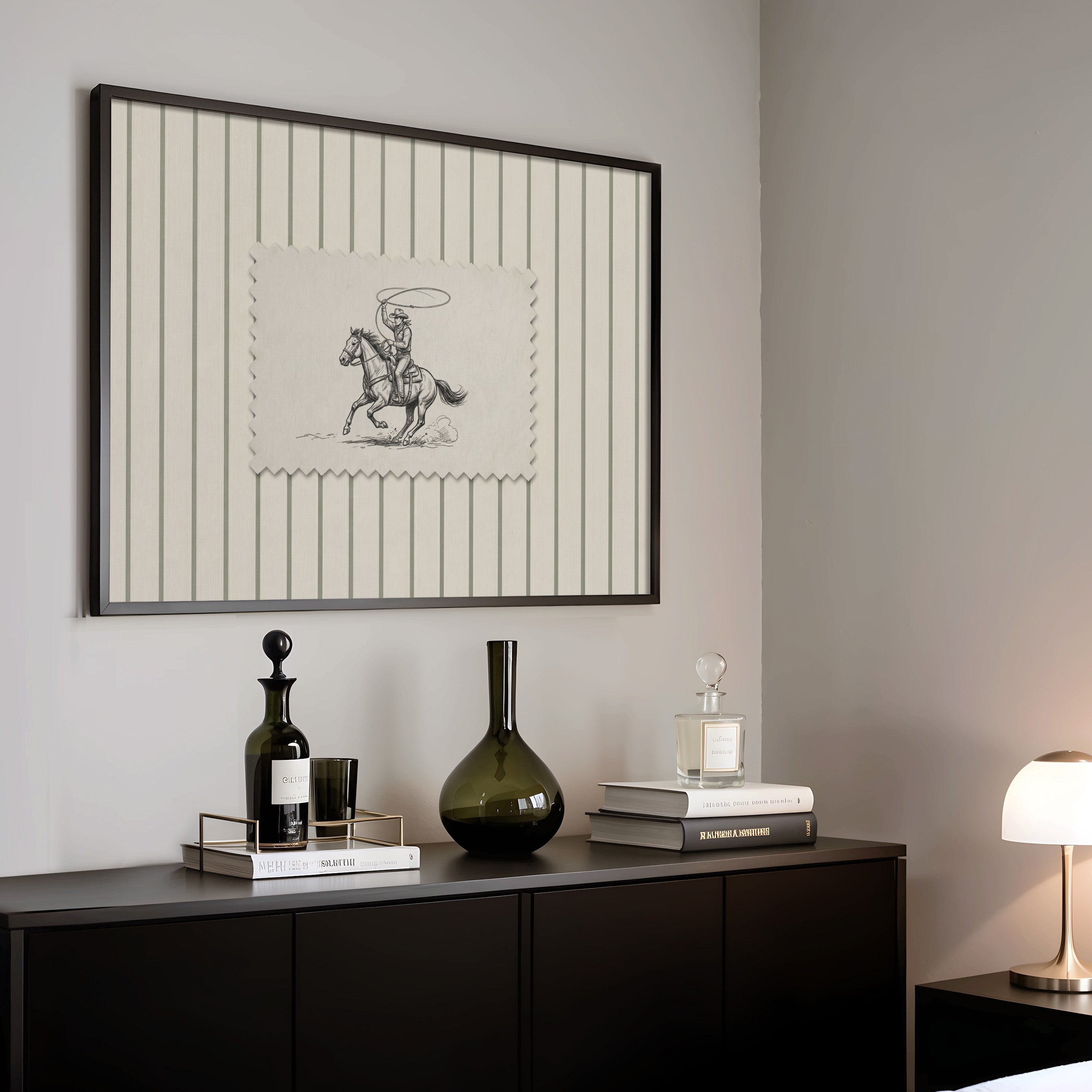 a black and white framed picture of a cowboy on a horse, a black vase, a stack of books, and a lamp on a black dresser.