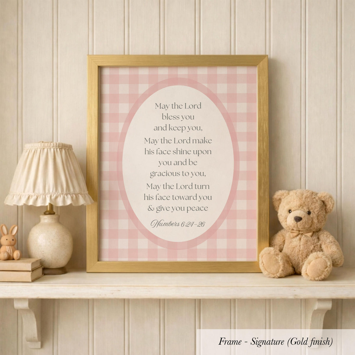 A framed Bible verse with a pink and white checkered background, accompanied by a teddy bear and a lamp on a shelf.