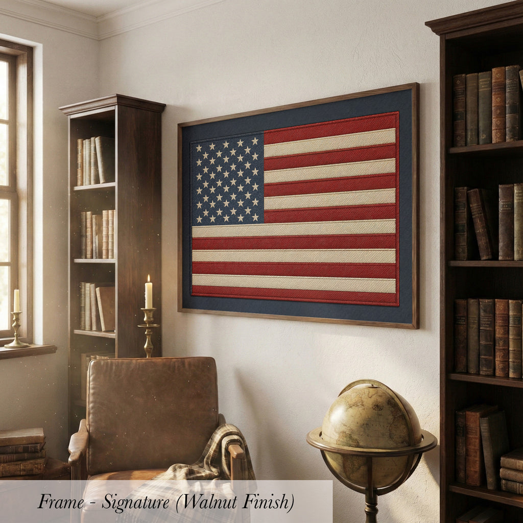 a large framed American flag hanging on the wall of a room with a leather chair, a globe, and a bookshelf filled with books.