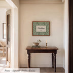 a wooden table with a bowl and a candle on it, set against a white wall with a framed picture hanging above it.