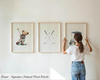 A woman is hanging three framed pictures on a wall.