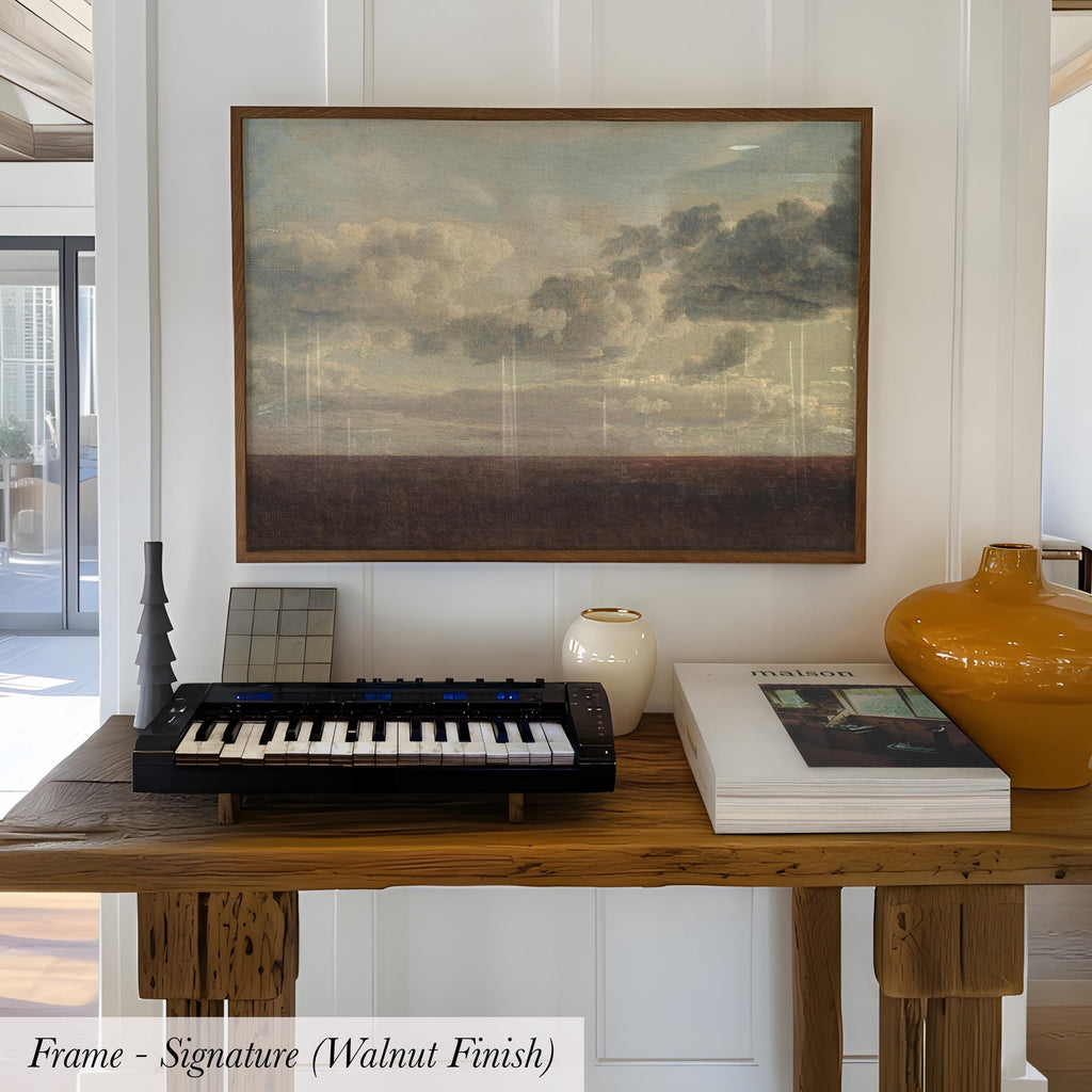 a wooden table with a framed painting hanging above it, a black keyboard, a white vase, and a stack of books.
