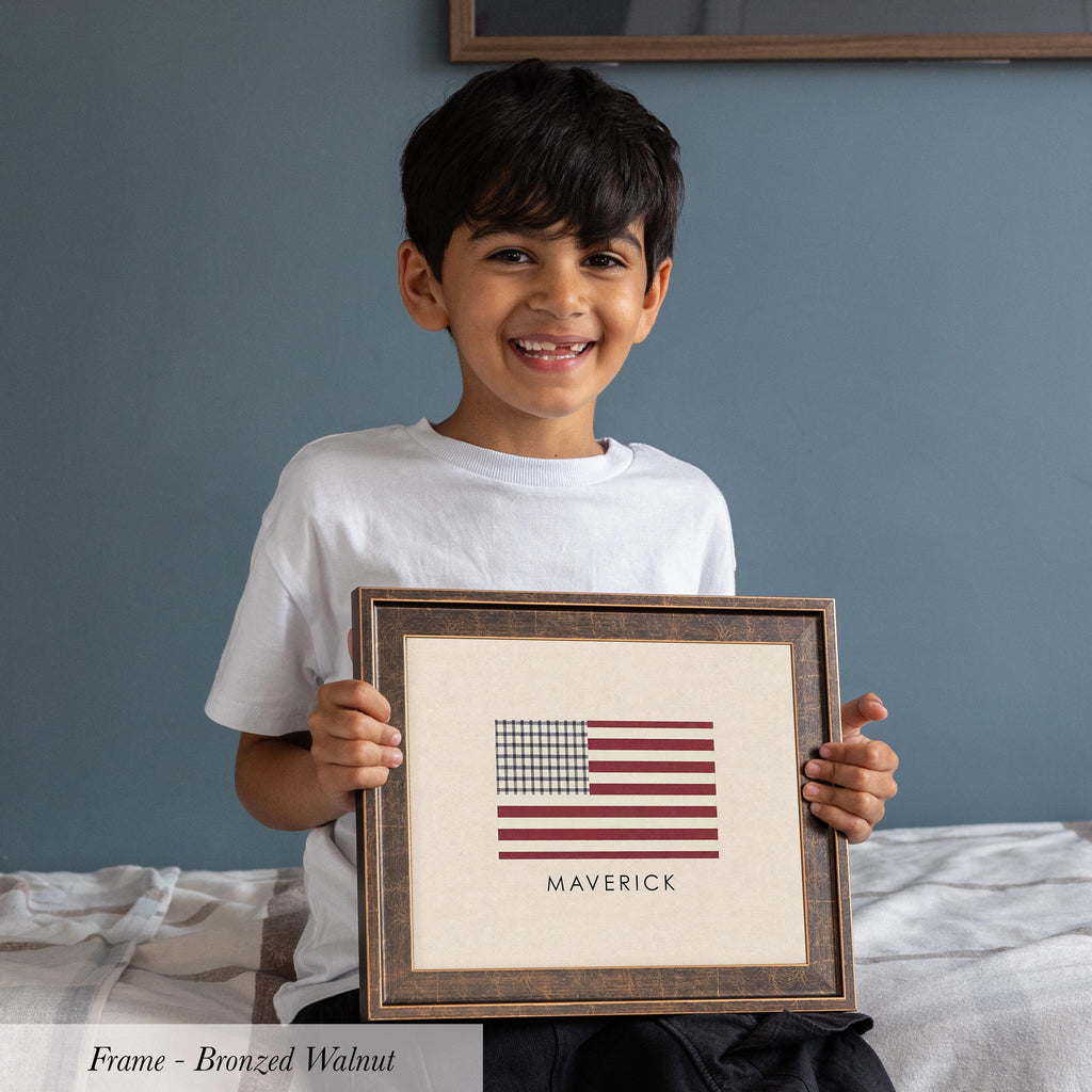 A young boy is holding a framed picture of the American flag and smiling.