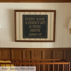 a framed cross-stitch design with the text "Every good & perfect gift is from above JAMES 1:17" on it, hanging on a wall above a wooden crib.