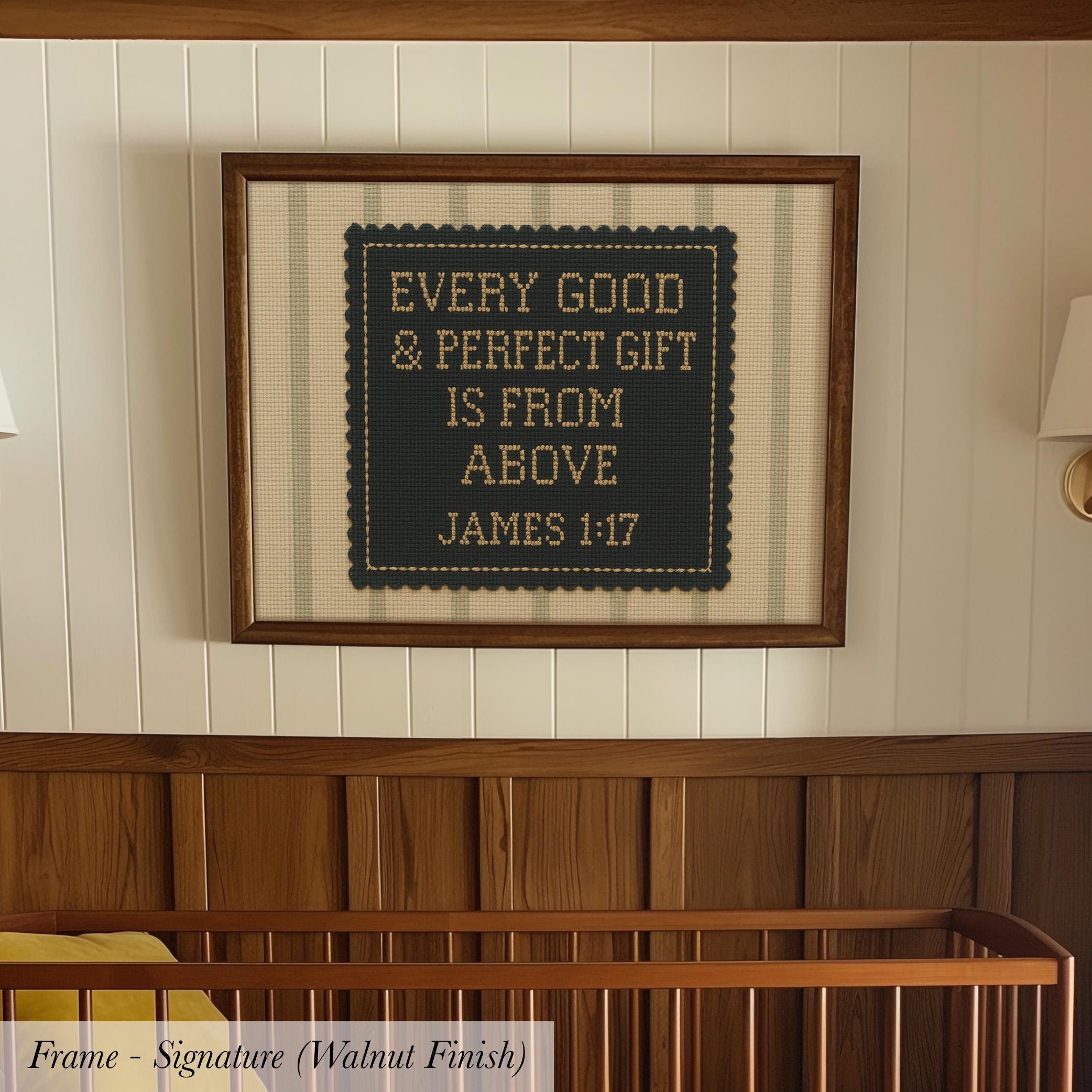 a framed cross-stitch design with the text "Every good & perfect gift is from above JAMES 1:17" on it, hanging on a wall above a wooden crib.