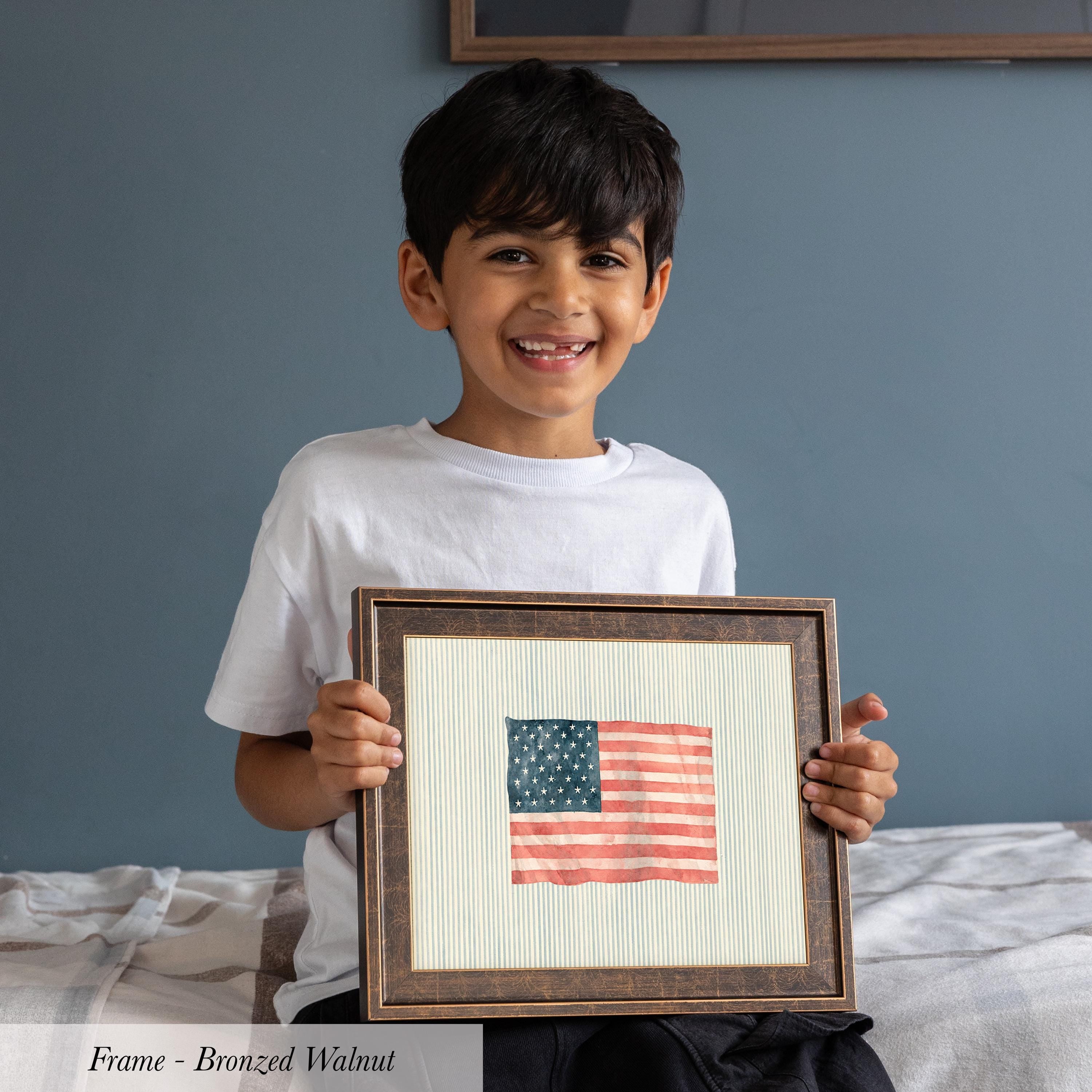 A young boy is holding a framed picture of an American flag, smiling and proudly displaying it.