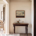 a wooden table with a bowl and a candle on it, set against a white wall with a framed landscape painting hanging above it.