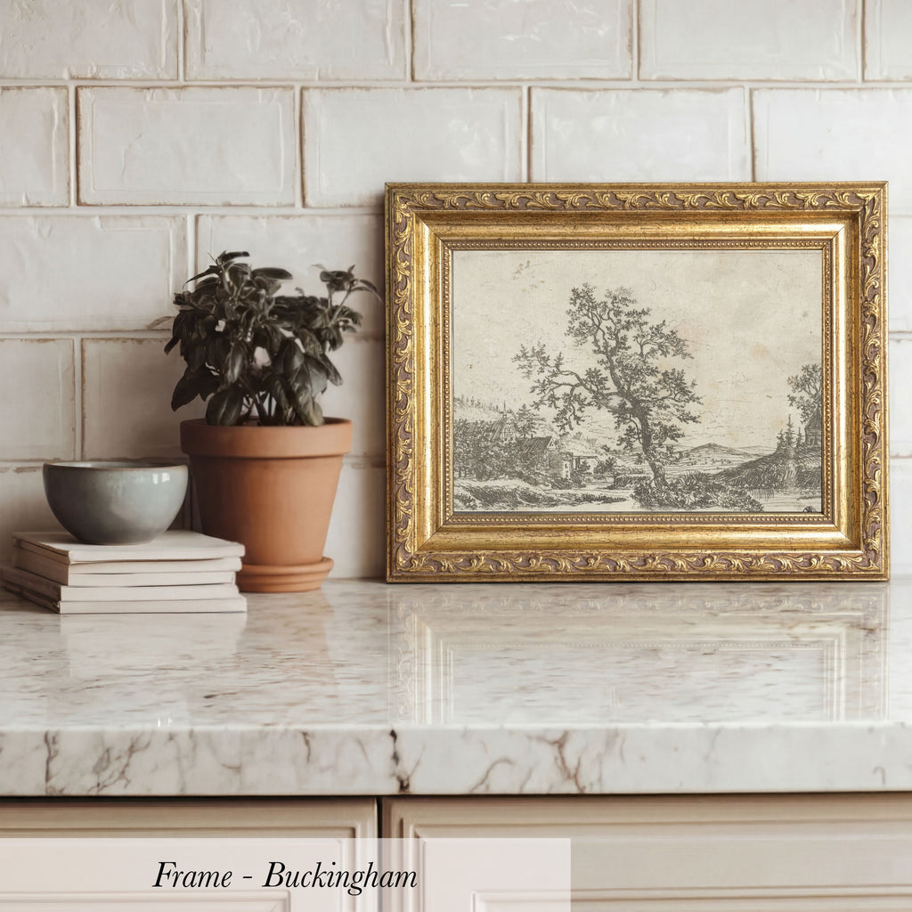 A framed landscape painting is displayed on a marble countertop, accompanied by a potted plant, a stack of books, and a bowl.