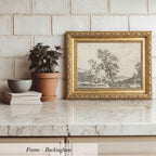A framed landscape painting is displayed on a marble countertop, accompanied by a potted plant, a stack of books, and a bowl.