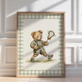 A framed watercolor painting of a teddy bear holding a lacrosse stick, wearing a green outfit and shoes, standing on a grassy surface.