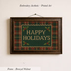A framed embroidered design with the text "HAPPY HOLIDAYS" on a green plaid background, hanging on a wall.