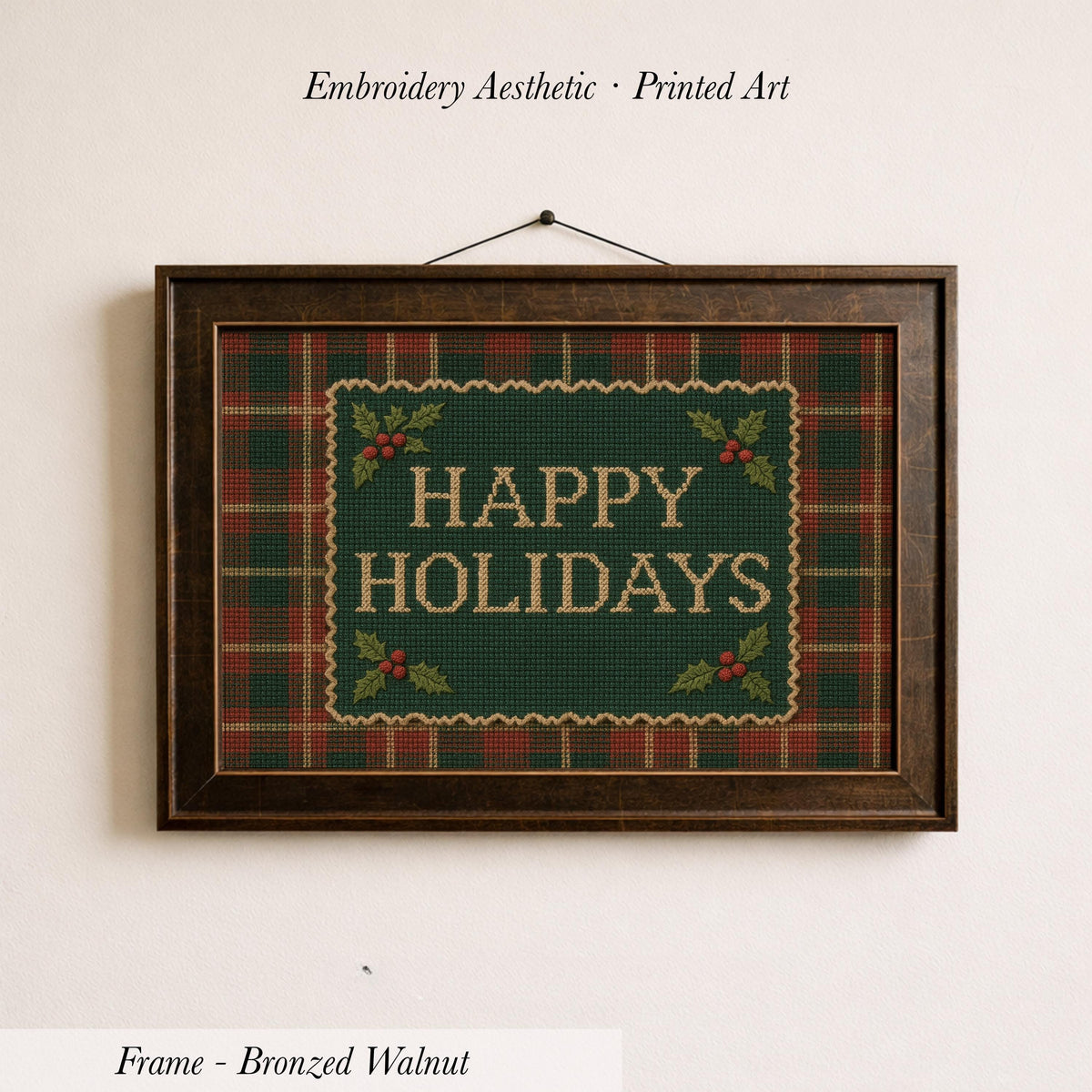 A framed embroidered design with the text "HAPPY HOLIDAYS" on a green plaid background, hanging on a wall.