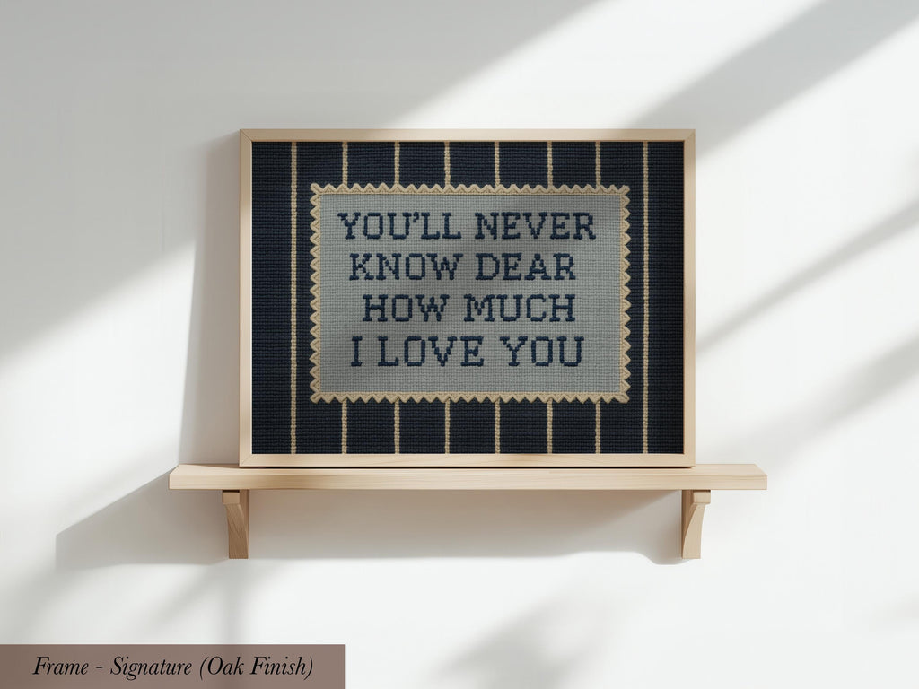 a framed cross-stitch design with the text "YOU'LL NEVER KNOW DEAR HOW MUCH I LOVE YOU" displayed on it.