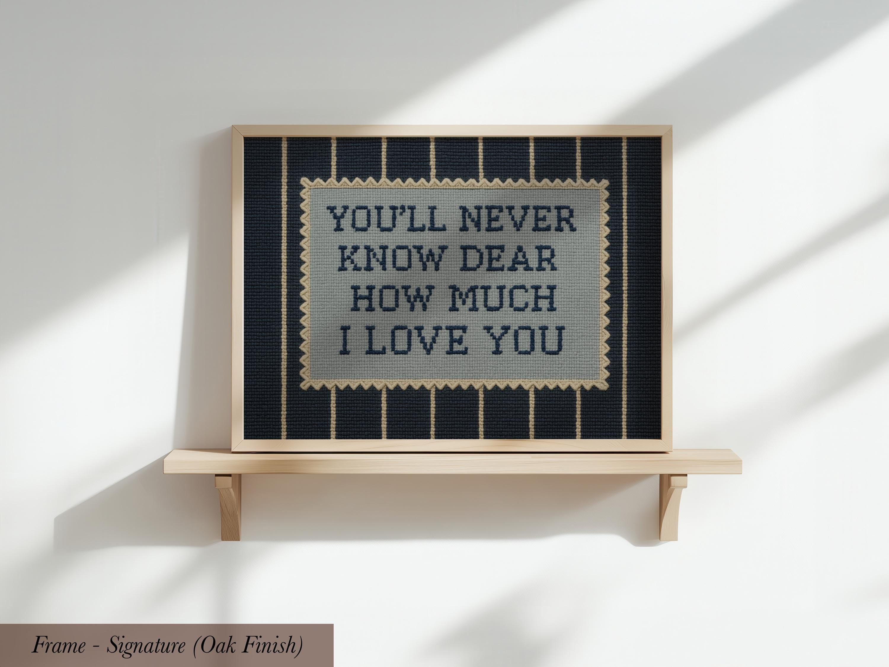 a framed cross-stitch design with the text "YOU'LL NEVER KNOW DEAR HOW MUCH I LOVE YOU" displayed on it.