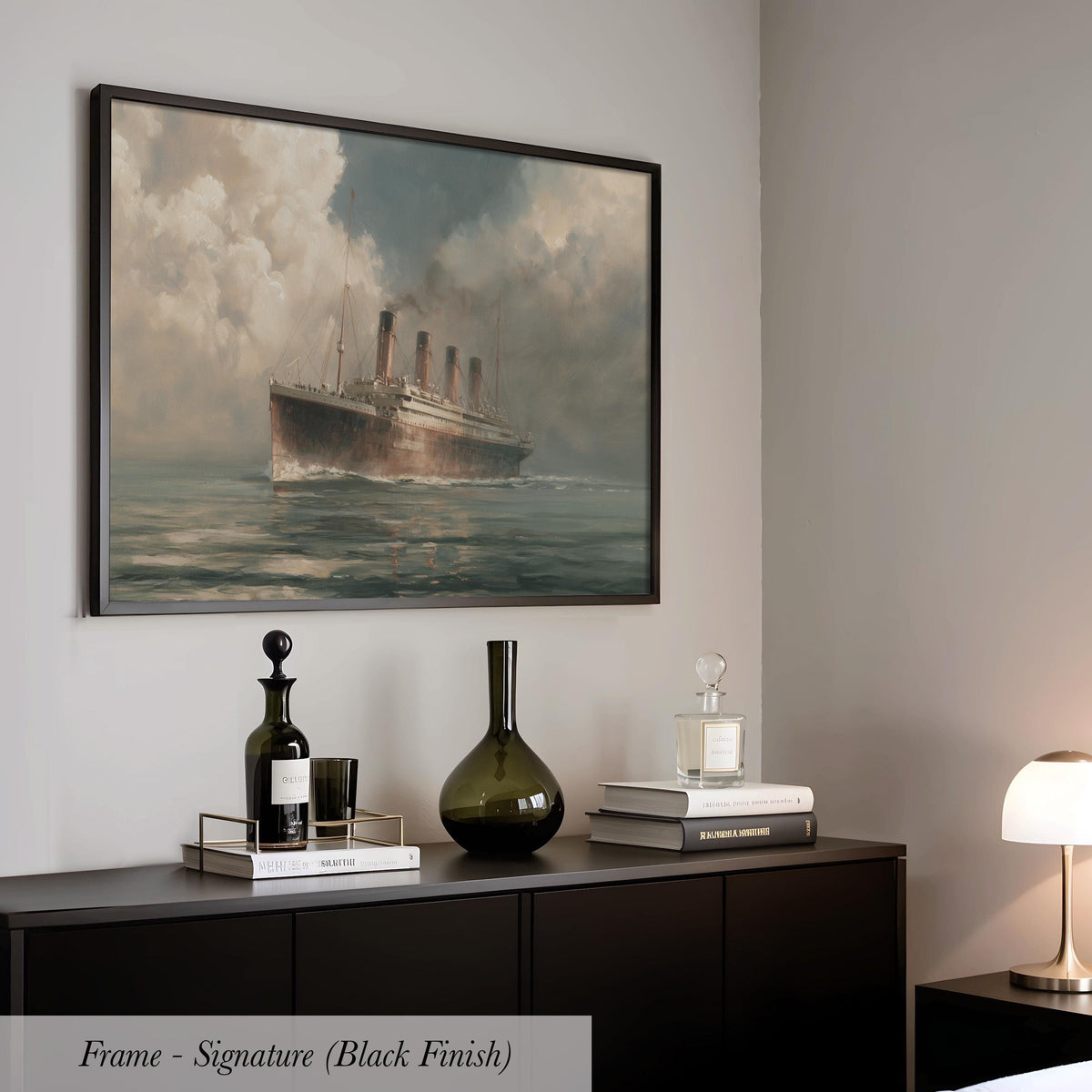 a framed painting of a large ship sailing on the ocean, with a black finish. The painting is hanging on a wall above a black cabinet or dresser, which has various items on top, including a bottle, a vase, and some books.
