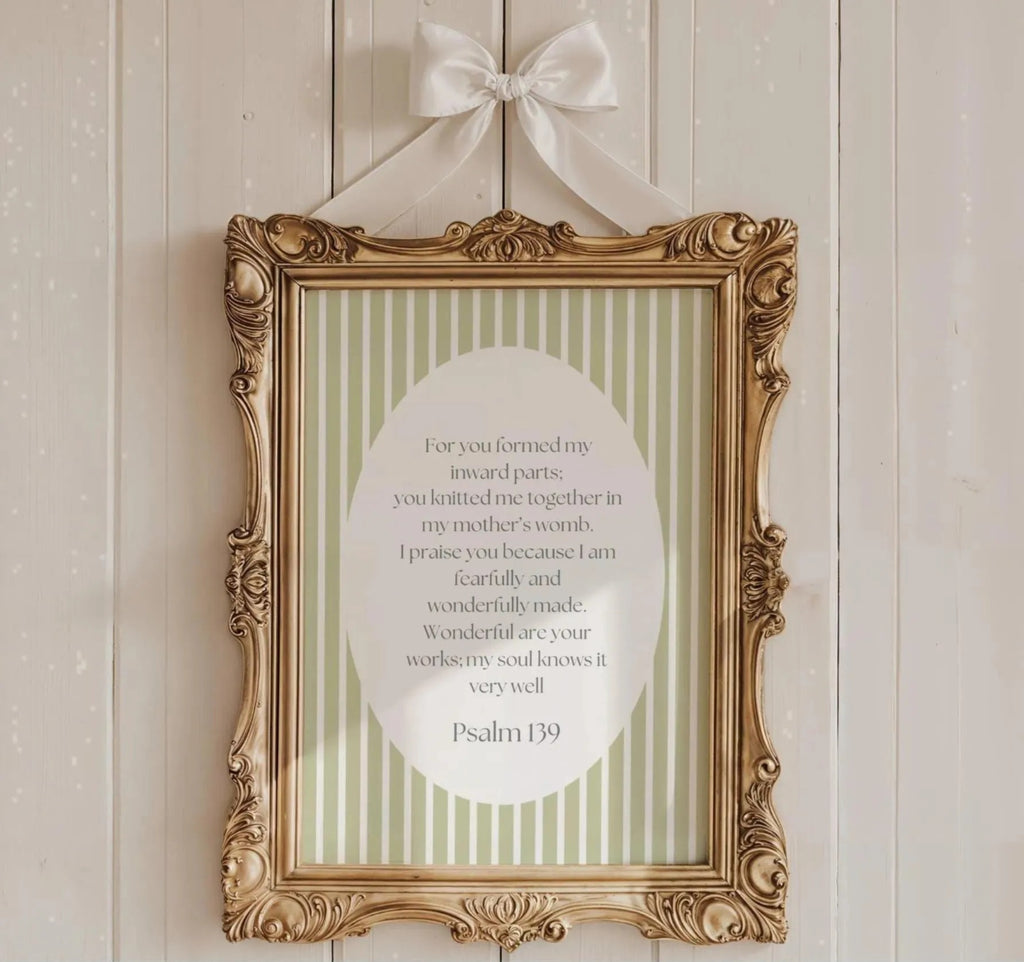 a gold-framed picture hanging on a white wall, displaying a green and white striped background with a white oval containing a poem or message.