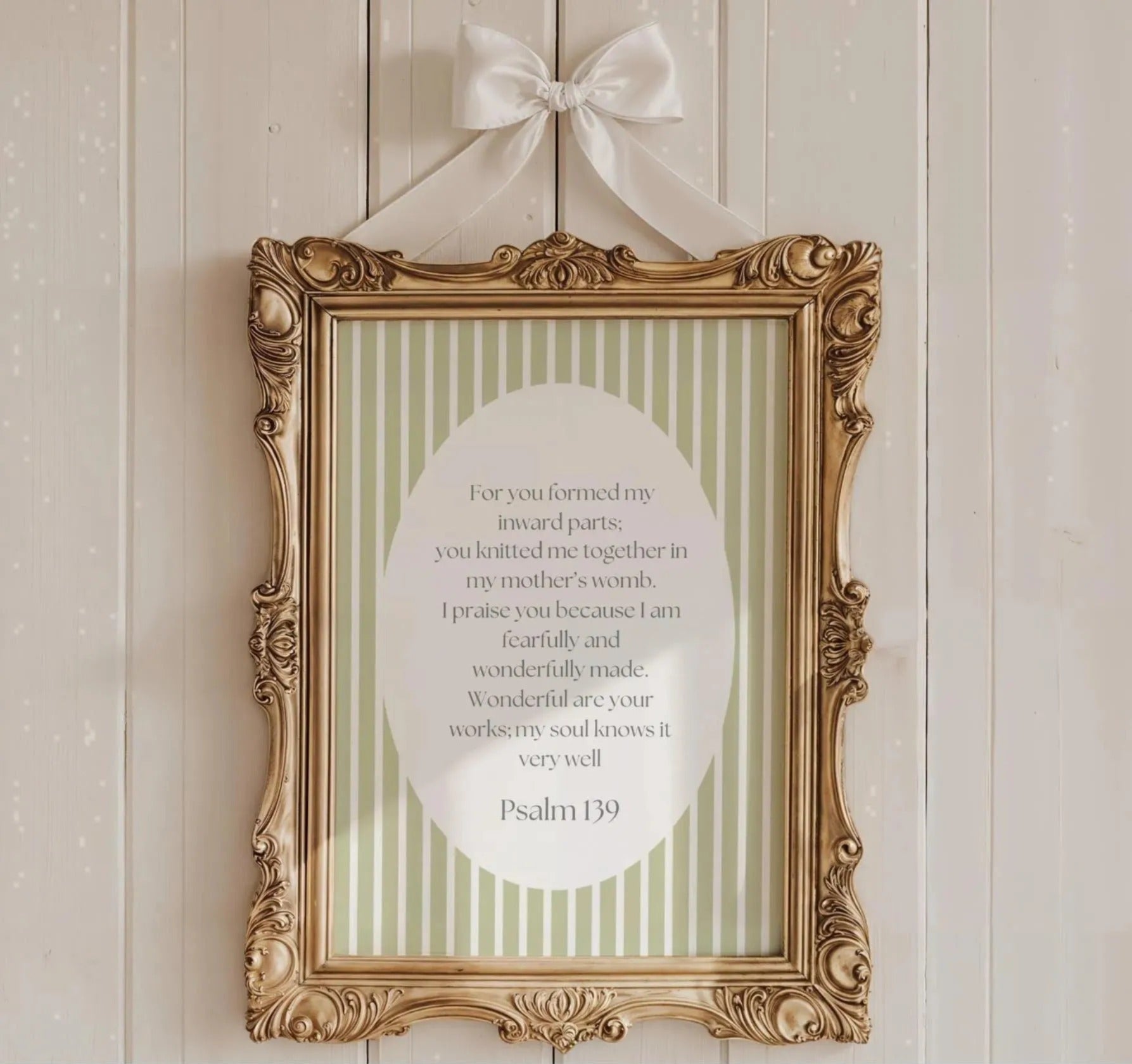 a gold-framed picture hanging on a white wall, displaying a green and white striped background with a white oval containing a poem or message.