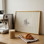 a wooden table with a framed picture of a cowboy on a horse, a croissant, and a cup of coffee.