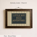 a framed embroidered design with the text "LITTLE BOY BIG ADVENTURES" on it.