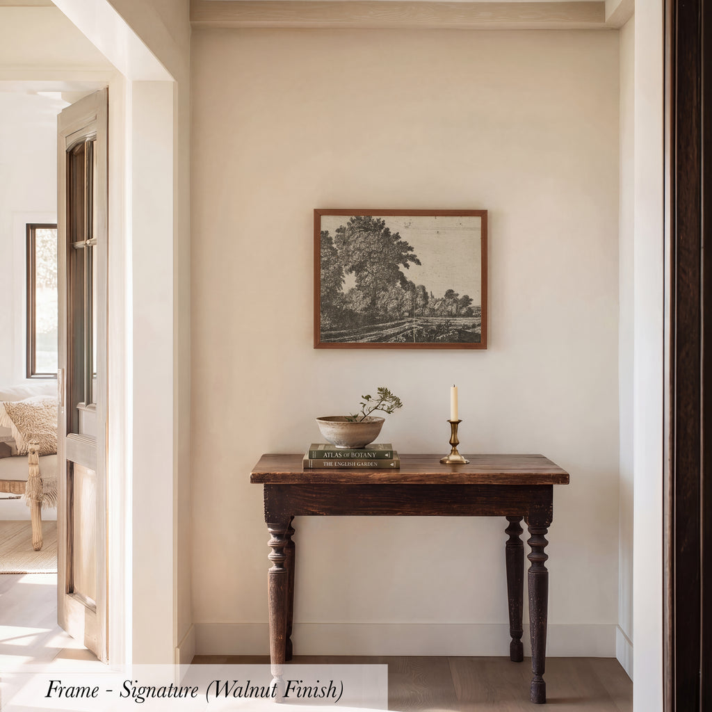 a wooden table with a bowl and a candle on it, set against a white wall with a framed picture hanging above it.