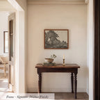 a wooden table with a bowl and a candle on it, set against a white wall with a framed picture hanging above it.