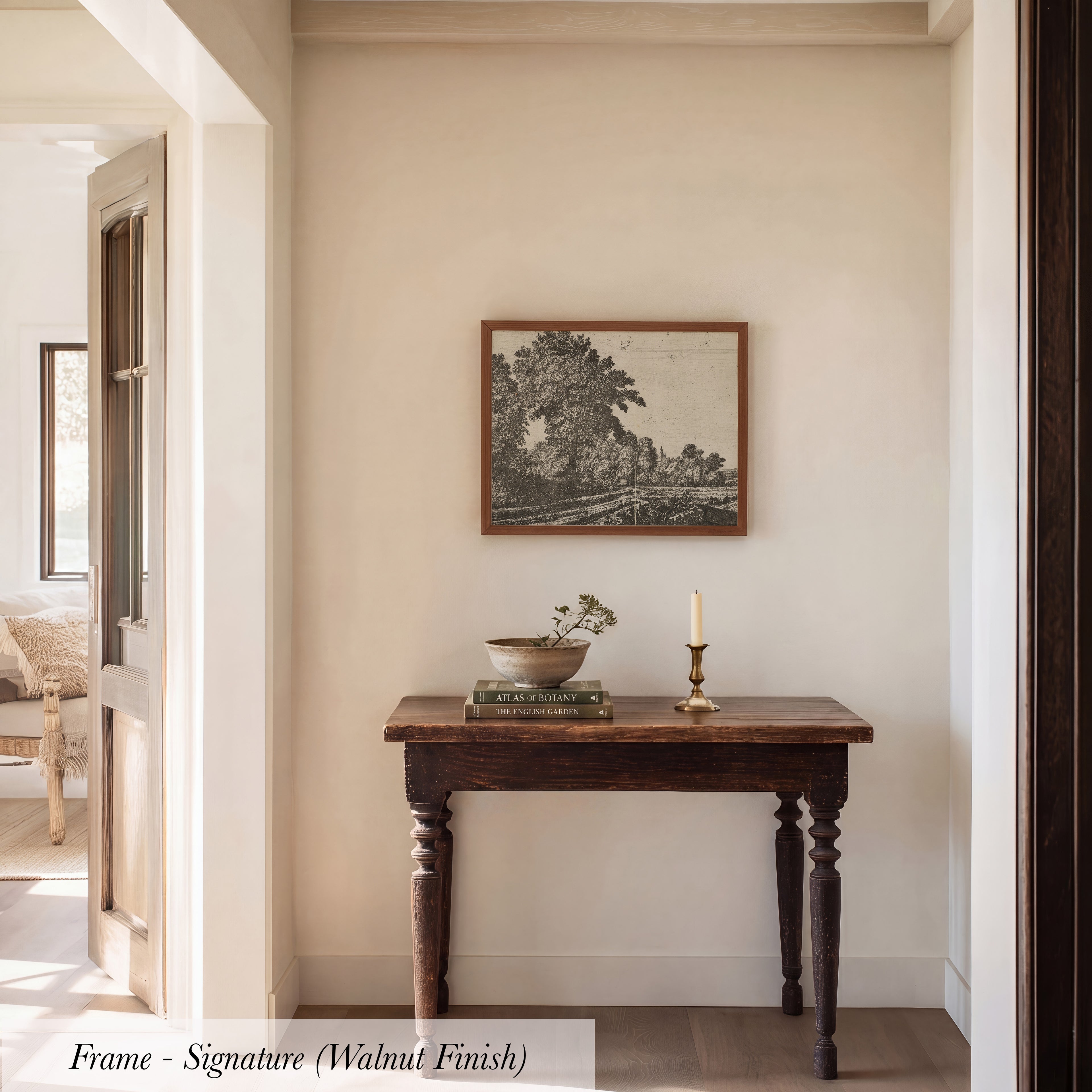 a wooden table with a bowl and a candle on it, set against a white wall with a framed picture hanging above it.