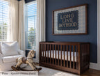 a nursery room with a wooden crib, a rocking horse, and a framed sign on the wall that reads "Long Live Boyhood".