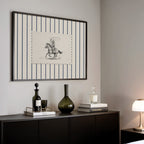 a black and white striped picture frame hanging on a wall above a black cabinet with various items on top, including a bottle, a vase, and a stack of books.