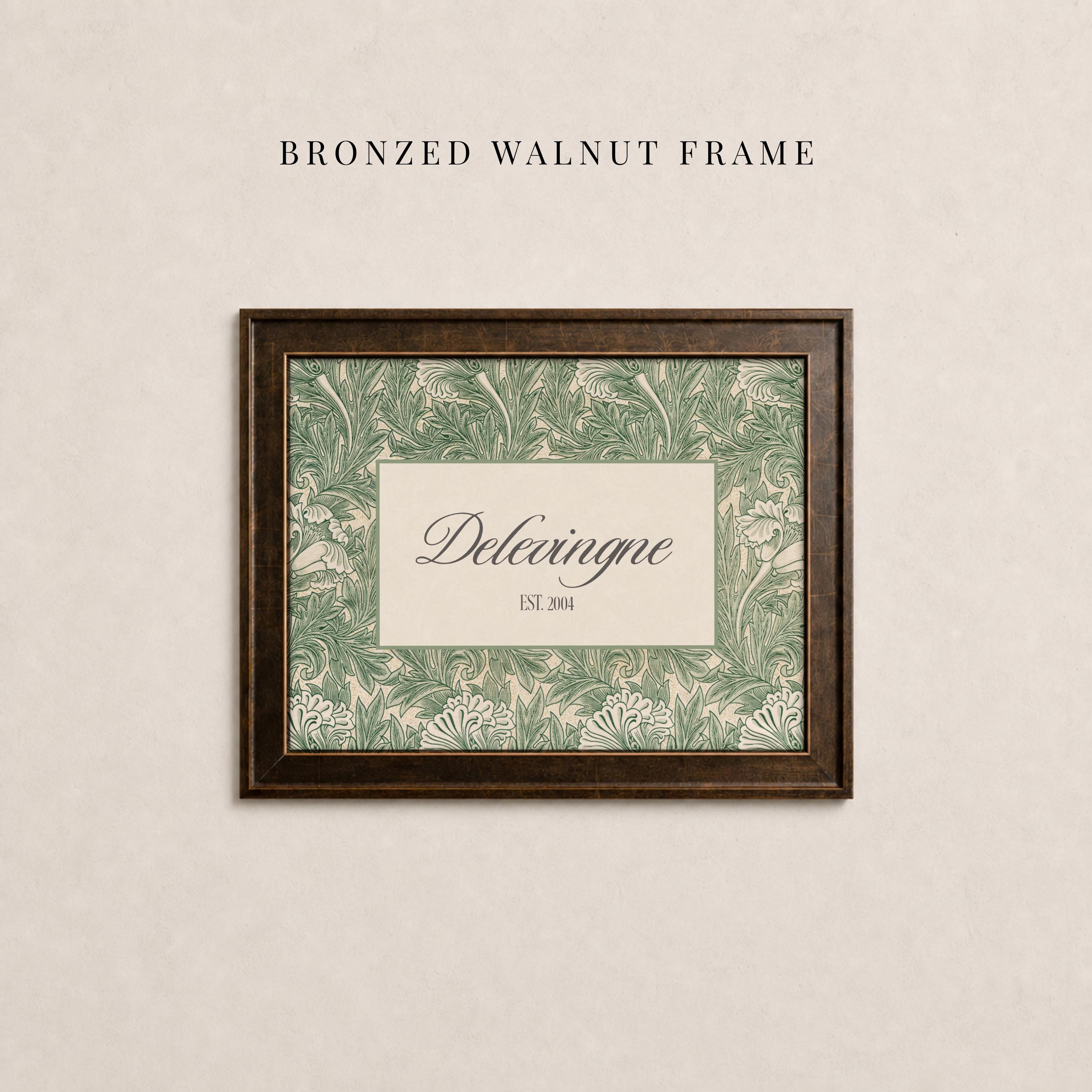 May include: A rectangular bronzed walnut frame containing a print with a green and cream botanical leaf pattern. The center features a cream rectangular inset with the text Delevingne and EST. 2004 printed in a dark serif font.