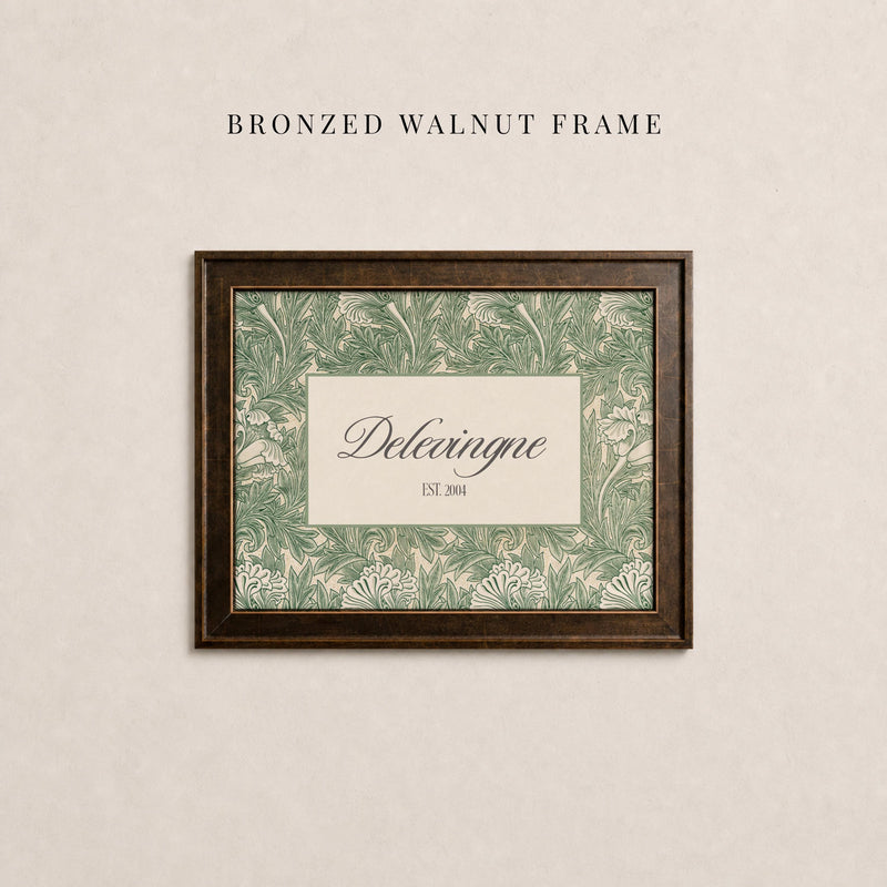 May include: A rectangular bronzed walnut frame containing a print with a green and cream botanical leaf pattern. The center features a cream rectangular inset with the text Delevingne and EST. 2004 printed in a dark serif font.