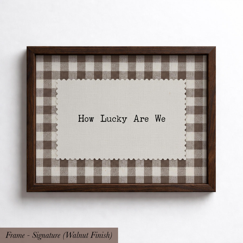 A framed piece of art with a checkered fabric border and a piece of paper inside the frame displaying the text "How Lucky Are We".