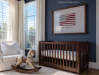 a nursery with a wooden rocking horse, a crib, and a framed American flag on the wall.