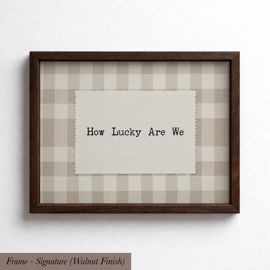 A framed picture with a piece of fabric inside the frame, displaying the text "How Lucky Are We" in a checkered pattern.