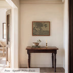 a wooden table with a bowl and a candle on it, set against a white wall with a framed picture hanging above it.