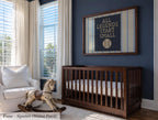 A nursery room with a wooden crib, a rocking chair, and a framed wall art with the text "ALL LEGENDS START SMALL".