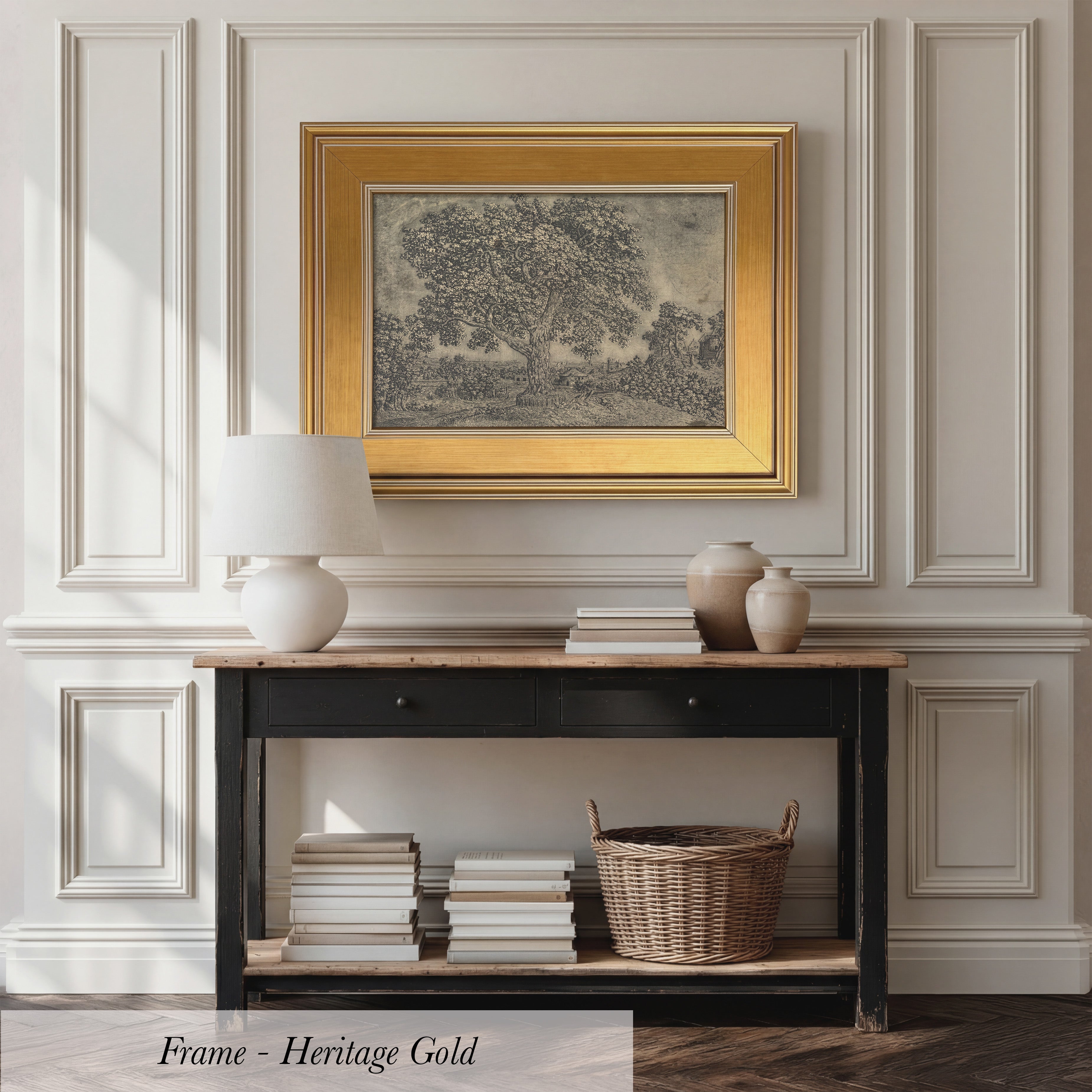 a black console table with a wicker basket, a stack of books, and a framed painting above it. The painting is in a gold frame and depicts a tree. The table is set against a white wall with a decorative molding.