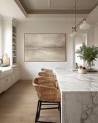 May include: A modern kitchen with a large abstract landscape painting in a gold frame. Three woven rattan bar stools with black metal legs sit in front of a marble countertop. A vase of greenery and fruit adds a natural touch.